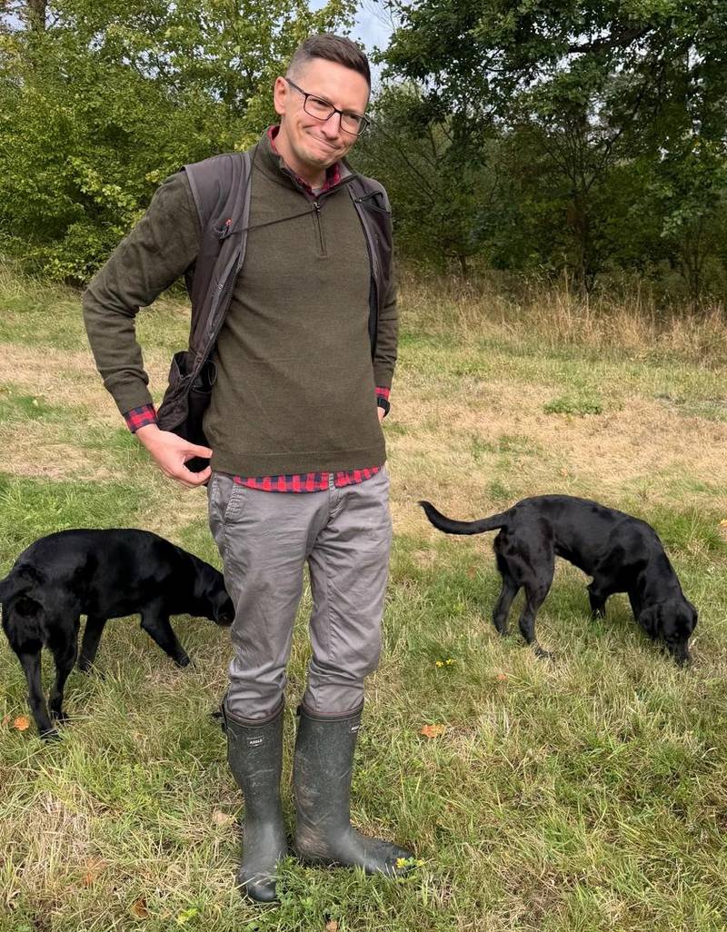 Sascha steht in der Mitte einer Wiese, links schnüffelt Femmy im Gras, rechts Corwin.